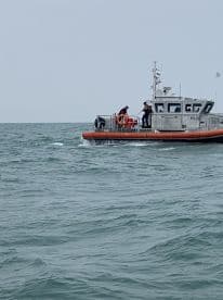 A U.S. Coast Guard boat is seen navigating through choppy waters, with crew members engaged in operations.