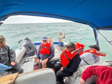 Group of anglers seated inside a boat, wearing life jackets, as they prepare for a fishing trip in open waters.