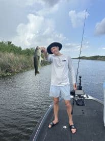 An angler proudly displaying a large Largemouth Bass while fishing on a calm waterway, showcasing a successful day on the boat.