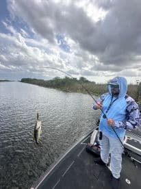 Angler reeling in a large Largemouth Bass while fishing in a scenic waterway, showcasing the excitement of freshwater fishing.