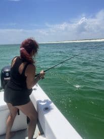 An angler reeling in a fish while fishing from a boat in clear, sunny waters, showcasing an exciting moment on the water.