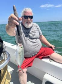 An angler proudly displaying a small fish while fishing on a boat in sunny waters.