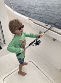 A young angler is actively fishing on a boat, showcasing enthusiasm while holding a fishing rod in a sunny environment.