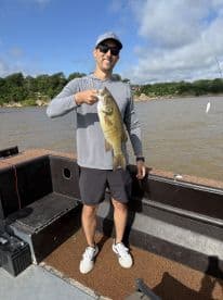 An angler proudly displaying a large Largemouth Bass while fishing on a boat, surrounded by a scenic lake environment.