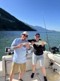 Two anglers proudly displaying their catch of the day, a pair of salmon, while enjoying a sunny day on the water.