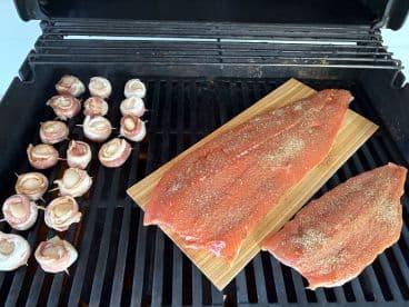 Freshly prepared salmon fillets and scallops wrapped in bacon on a grill, showcasing a delicious seafood meal ready for cooking.