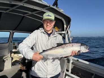 An angler proudly displaying a large Salmon aboard a fishing boat, enjoying a successful day on the water.