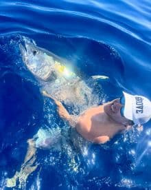 Angler reeling in a large Yellowfin Tuna while enjoying a deep-sea fishing adventure in clear blue waters.