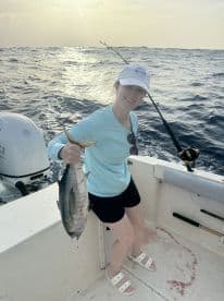 An angler proudly displaying a large fish while fishing on a boat in open waters, showcasing a successful catch during a sunny day.