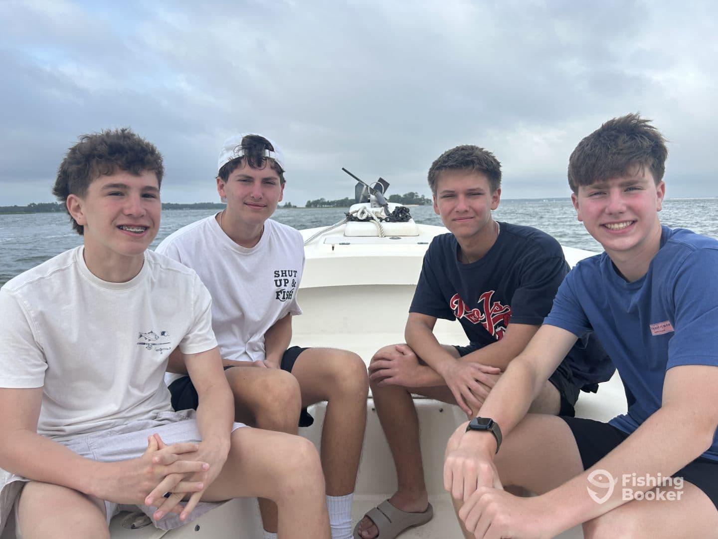Four young anglers seated inside a boat, enjoying a day on the water, with a scenic backdrop of the coastline.