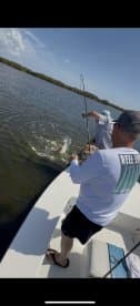 Two anglers engaged in an exciting fishing moment, reeling in a fish in a scenic mangrove environment.