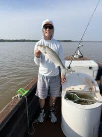 An angler proudly displaying a striped bass while fishing from a boat in a calm waterway.