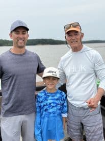 A family group posing on a boat, enjoying a fishing trip on a calm waterway.