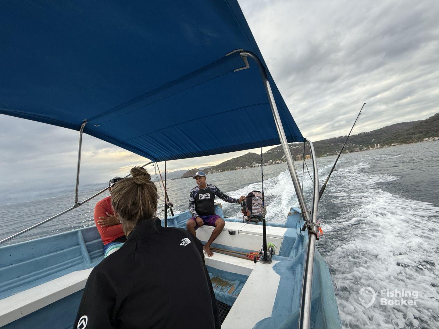 Interior view of a small fishing boat with anglers seated, cruising along a coastal waterway, showcasing a relaxed fishing atmosphere.