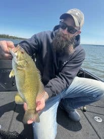 An angler proudly displaying a large Largemouth Bass while fishing on a serene lake.