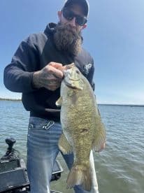Angler proudly displaying a large Smallmouth Bass while fishing on a calm lake.