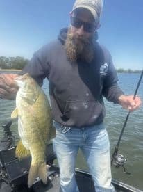 Angler displaying a large Smallmouth Bass while fishing on a lake, showcasing a successful catch in a serene environment.