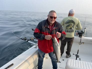 An angler proudly displaying a large fish while fishing on a boat, with calm waters in the background.