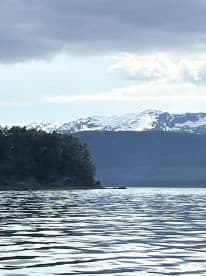 A scenic view of a mountainous coastline with snow-capped peaks reflecting on calm waters, ideal for fishing adventures.