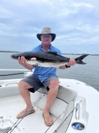 An angler proudly displaying a large shark caught while fishing from a boat, showcasing the excitement of a successful fishing trip.