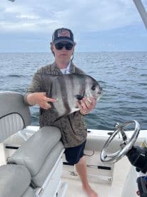 Young angler displaying a large fish aboard a boat in open waters, showcasing a successful fishing trip.