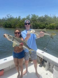 Two anglers proudly displaying their Snook catch while fishing in a scenic waterway.