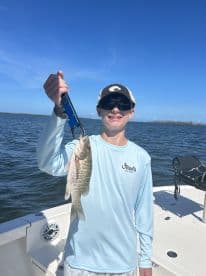 A young angler proudly displaying a freshly caught fish while on a boat in a scenic fishing environment.