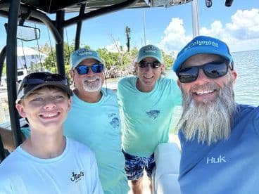 A cheerful group of anglers, including a young boy, poses for a selfie inside a fishing boat, showcasing a sunny day on the water.