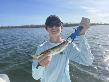 A young angler proudly displaying a Speckled Trout while fishing in a scenic waterway.