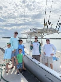 A family of five poses by their fishing boat at the dock, showcasing a beautiful day on the water.