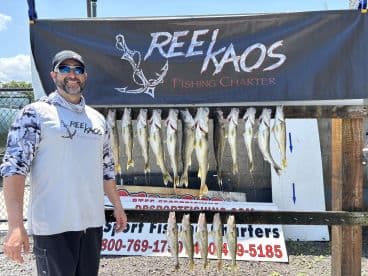 A smiling angler stands beside a display of freshly caught fish, showcasing a successful day with a charter service, featuring several large Walleye on a catch board.