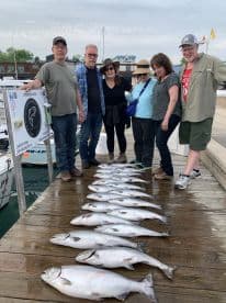 A group of anglers proudly displaying their catch of multiple Lake Trout on a dock after a successful fishing trip.
