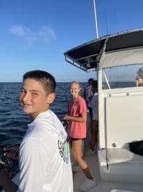 Two young anglers actively fishing on a boat, enjoying a sunny day on the water.