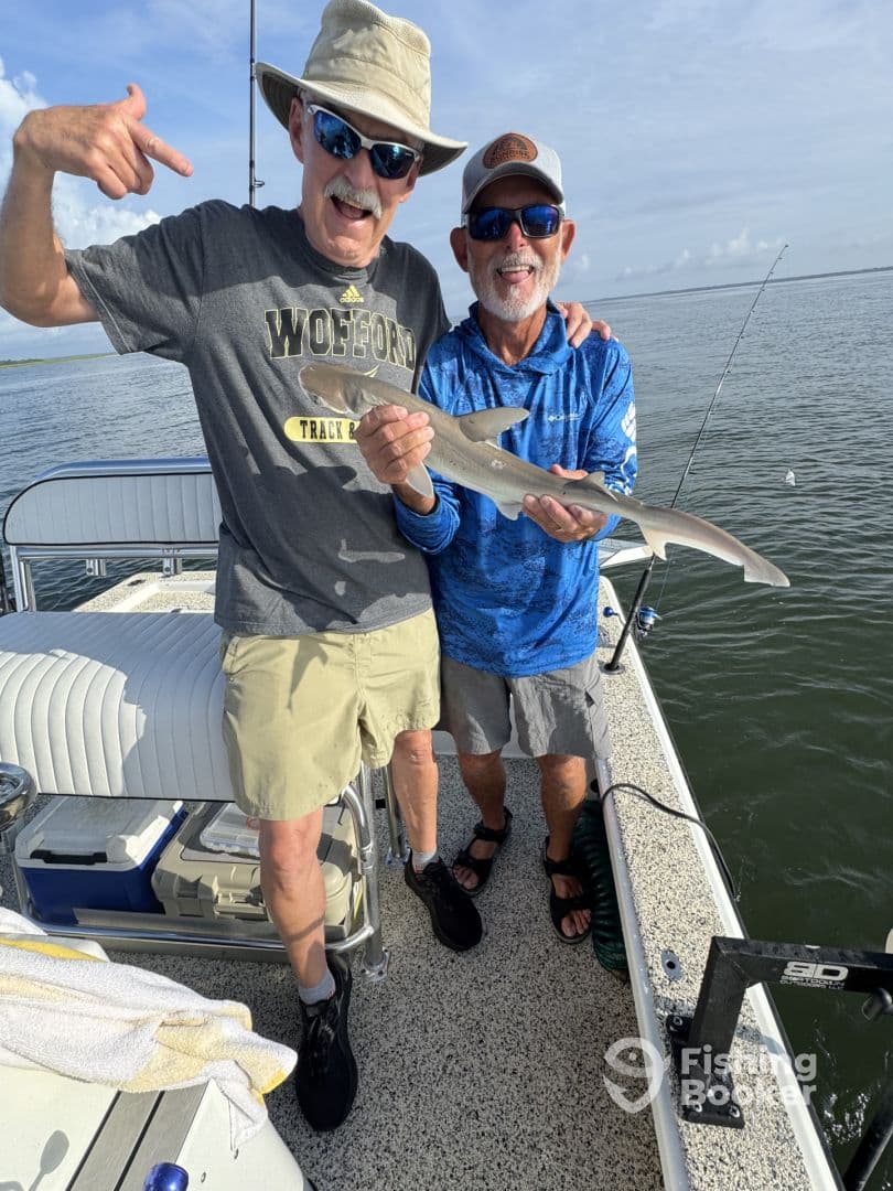 Two anglers proudly displaying a small shark caught during a fishing trip, showcasing a fun moment on the water.