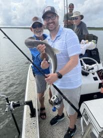 Two anglers proudly displaying a caught shark while fishing on a boat in a scenic waterway.