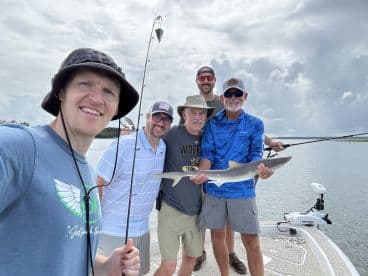 Group of anglers proudly displaying a caught shark while enjoying a day of fishing on the water.