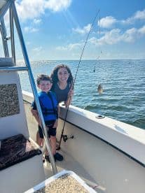A young boy and a woman enjoying a fishing trip on a boat, with the boy holding a fishing rod and a small catch visible.