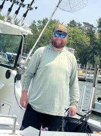 A smiling angler stands at the helm of a fishing boat, showcasing the vessel's interior features and a sunny day on the water.