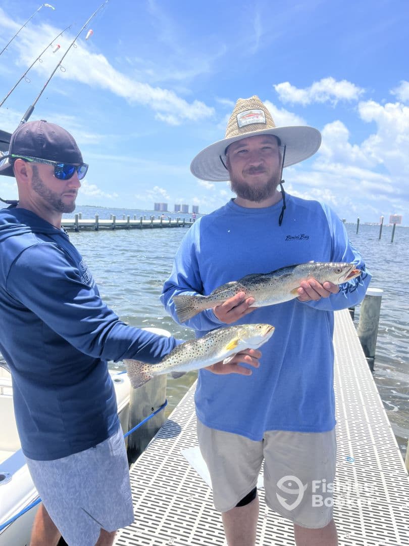 Two anglers proudly displaying their catches of Speckled Trout while docked, showcasing a successful day on the water.