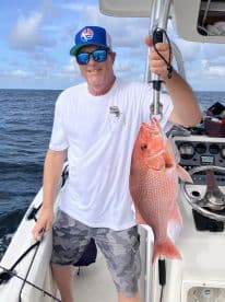An angler proudly displaying a large Red Snapper while fishing on a boat in open waters.