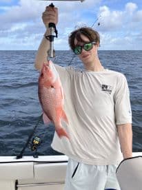 A young angler proudly displaying a freshly caught Red Snapper while fishing offshore, showcasing the excitement of a successful day on the water.