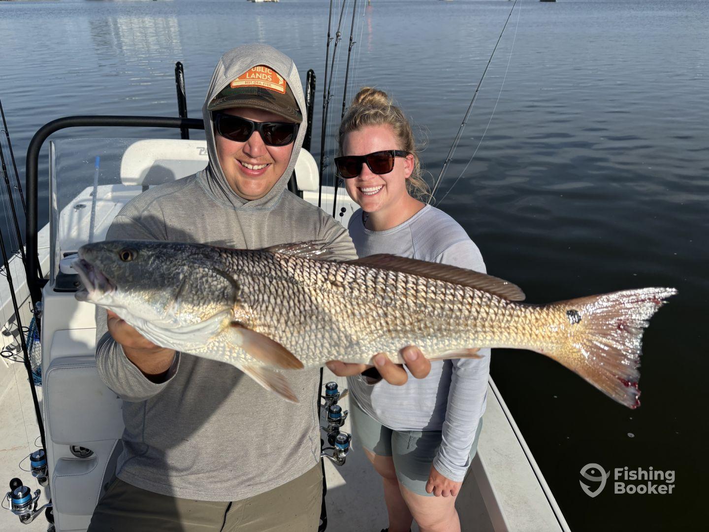 Two anglers proudly displaying a large Redfish on a boat during a fishing trip.