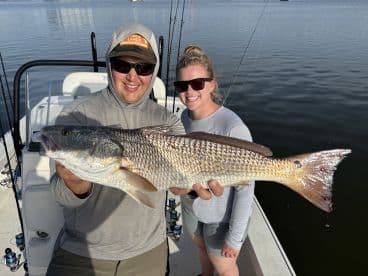 Two anglers proudly displaying a large Redfish on a boat during a fishing trip.