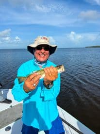 Angler proudly displaying a Speckled Trout while fishing on a sunny day in a coastal waterway.