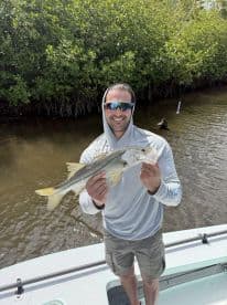 Angler proudly displaying a Snook caught while fishing in a mangrove area, showcasing a sunny day on the water.