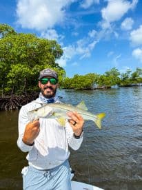 Angler proudly displaying a Snook caught while fishing in a mangrove area, showcasing a sunny day on the water.