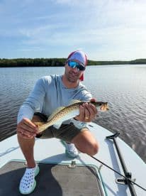 An angler proudly displaying a Speckled Trout while fishing on a calm waterway, showcasing a successful day on the water.