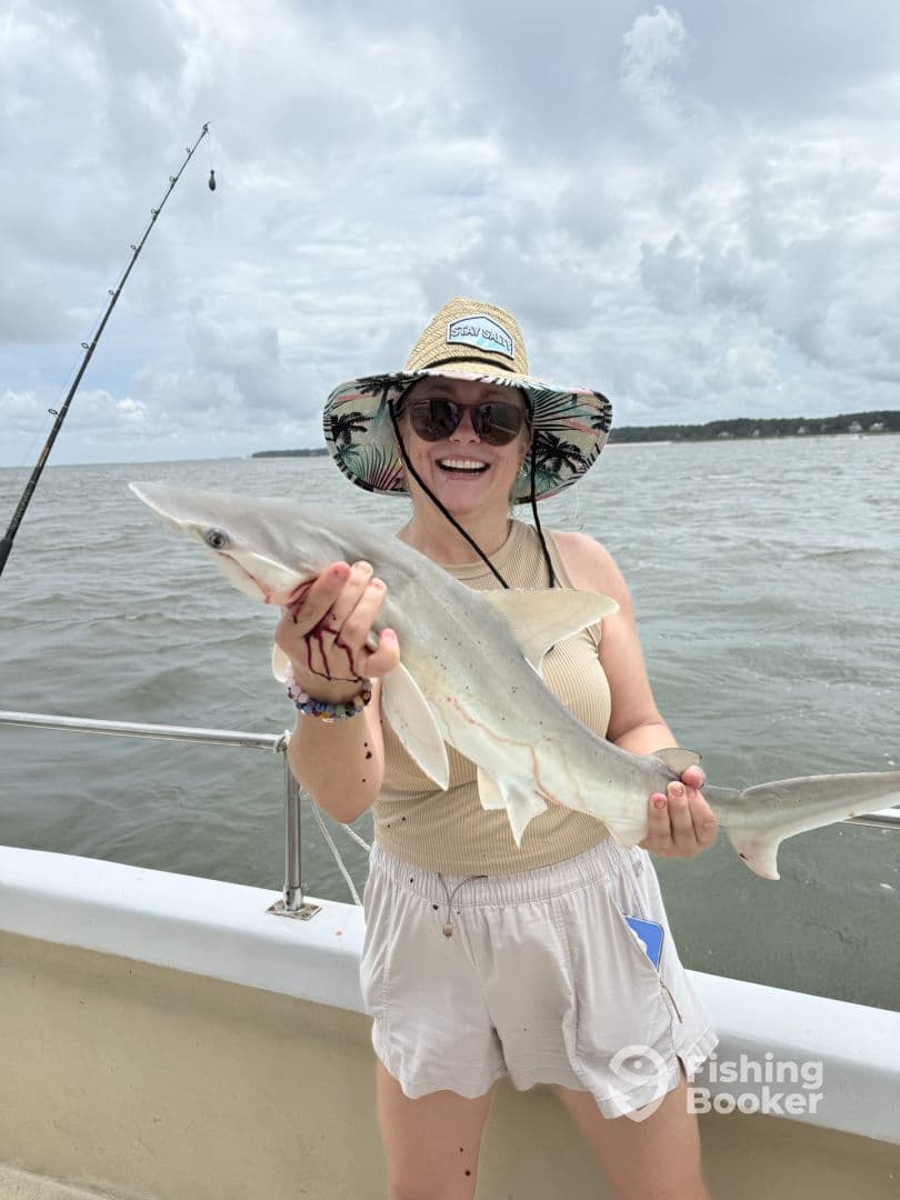 An excited angler proudly displaying a caught shark while fishing on a boat, showcasing a fun day on the water.