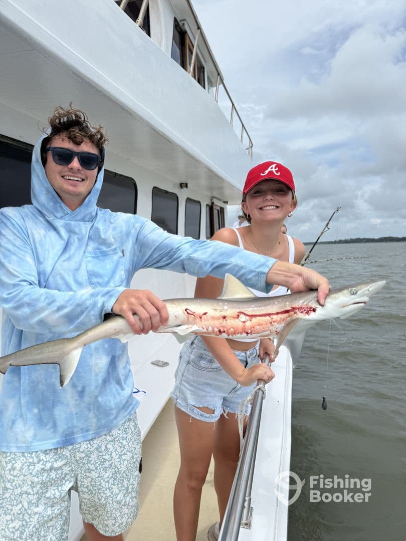 Two anglers proudly displaying a caught shark while on a fishing charter, showcasing a successful day on the water.
