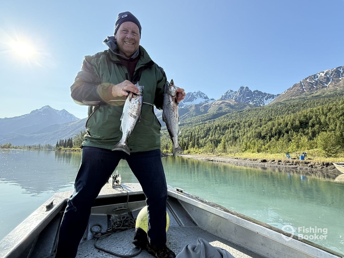 An angler proudly displaying two freshly caught fish while on a scenic boat trip in a mountainous region.